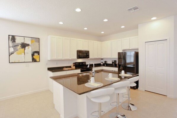 A modern kitchen with white cabinets, a central island with bar stools, a stainless steel refrigerator, and a microwave. - All Suite 5Bed/Baths -No Carpets-New Pics coming soon- Near Disney~ (Kissimmee)