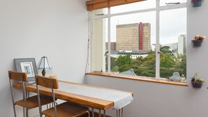 Et værelse med et træbord og stole, et vindue med udsigt til bygninger og plantekasser på vindueskarmen.