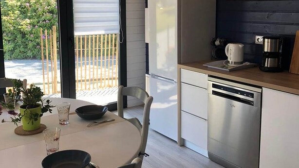 A modern kitchen with a wooden ceiling, a dining table with chairs, a refrigerator, a dishwasher, and a coffee maker. - Gîte "l'aiguille creuse (Criquebeuf-en-Caux)