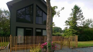 A modern two-story house with a wooden fence, surrounded by gravel and landscaped with various plants and flowers. - Gîte "l'aiguille creuse (Criquebeuf-en-Caux)