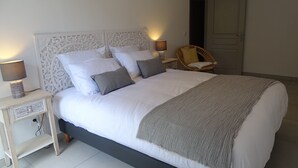 A neatly made bed with white linens and a grey throw, a bedside lamp, and a decorative wall headboard. - LUVA D'azur LE RIOU in the heart of the Grasse region (Le Bar-sur-Loup)