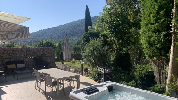 A hot tub in a garden with a stone wall, outdoor furniture, and a view of a hill. - LUVA D'azur LE RIOU in the heart of the Grasse region (Le Bar-sur-Loup)