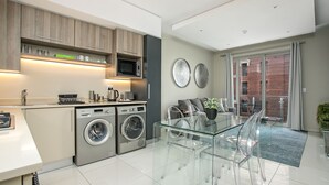A modern kitchen with built-in appliances, a glass dining table, and a view of the outside. - Designer Apartment in The Iconic Tyrwhitt (Johannesburg)
