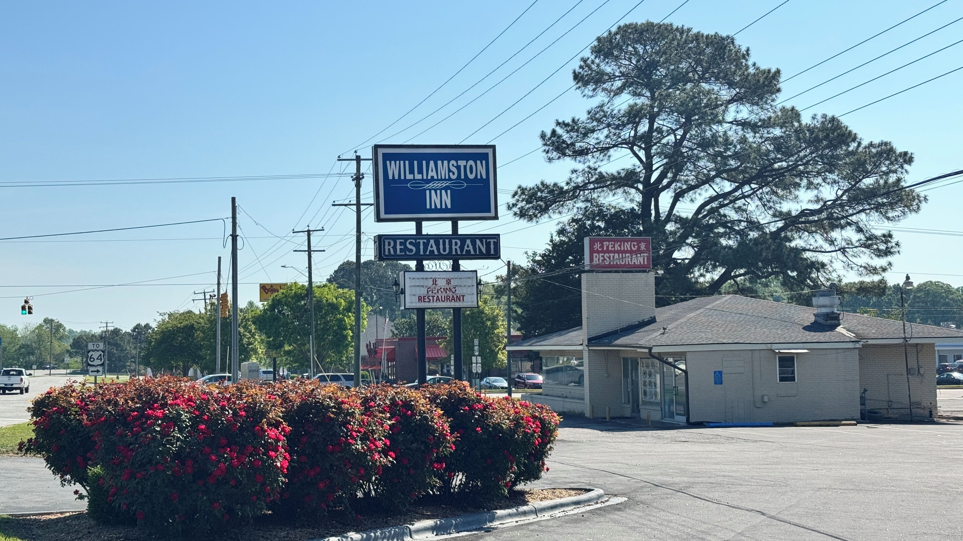A roadside sign for a Williamston Inn and two restaurants, with a parking lot and a building in the background.