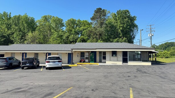 A motel with a single-story structure, a covered parking area, and a small outdoor seating area. - Williamston Inn NC Near Greenville US 64 (Williamston)