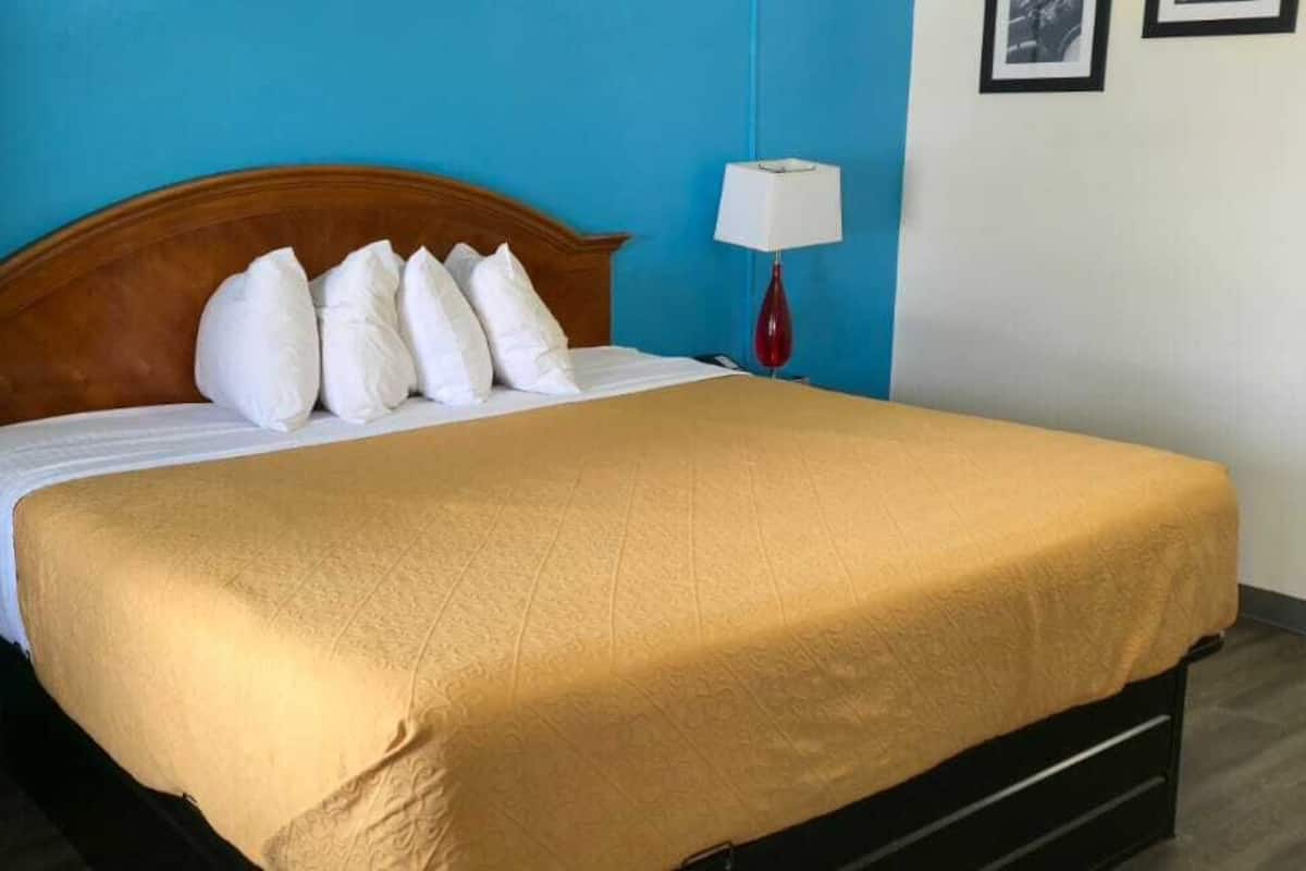 Un lit avec une tête de lit en bois, des oreillers blancs et une couvre-lit beige, dans une pièce aux murs bleus et au plancher en bois.
