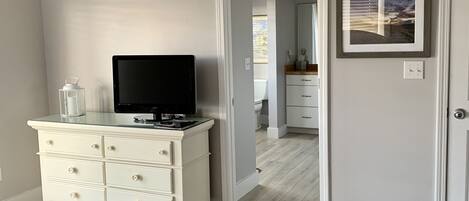 A bedroom with a bed, a dresser, a television, and a door leading to a bathroom.