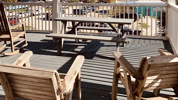 A wooden deck with benches and chairs, overlooking a beach and buildings in the distance.