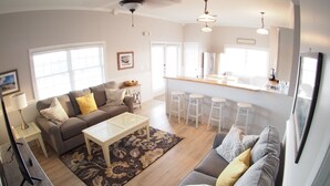 A modern living room with a grey sofa, a coffee table, and a kitchen area with bar stools.
