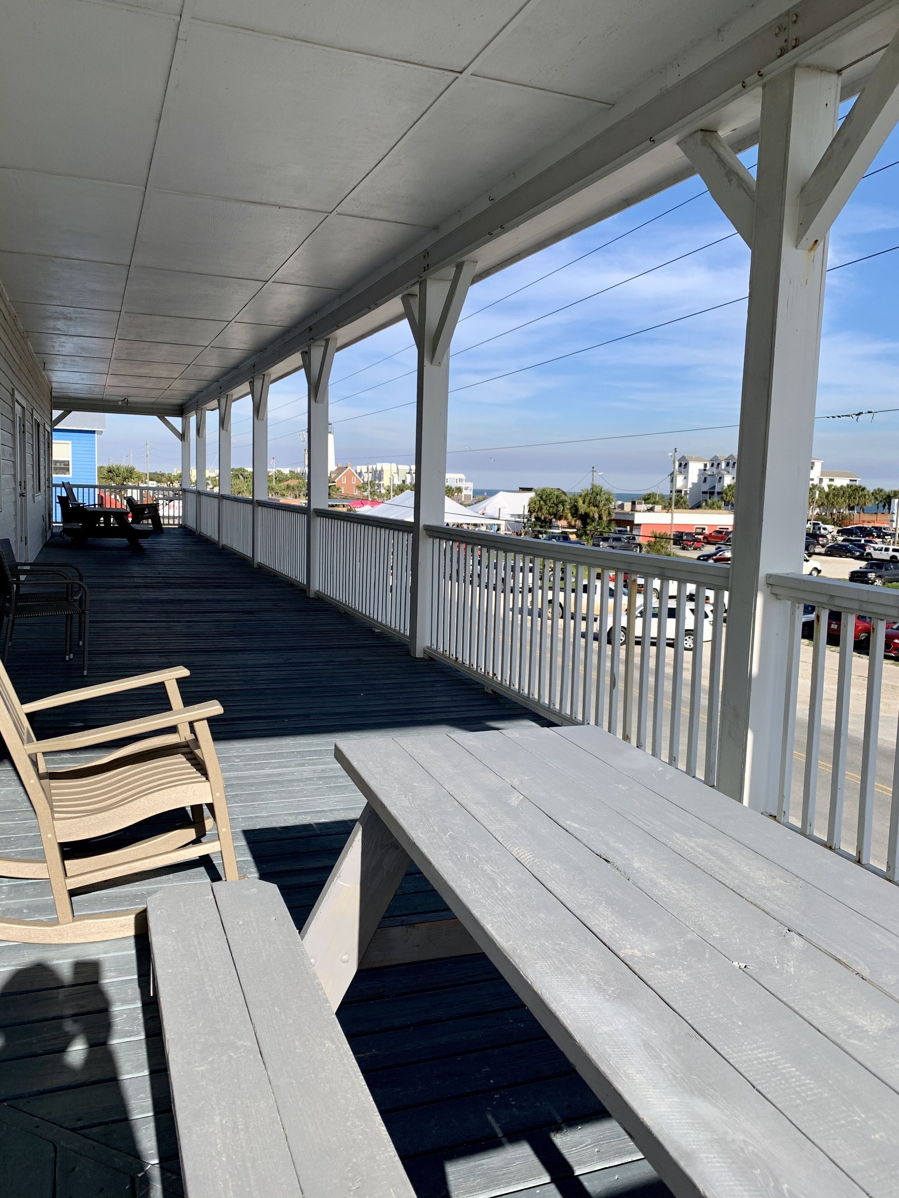A covered outdoor area with wooden benches and railings, overlooking a parking lot and buildings.