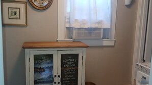 A bathroom with a shower, a framed picture, a cabinet with a chalkboard sign, and a window with curtains.