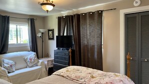 A bedroom with two beds, a dresser, a television, and a window with curtains.
