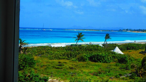 Vista de uma praia com águas azul-claras, palmeiras e uma tenda branca.