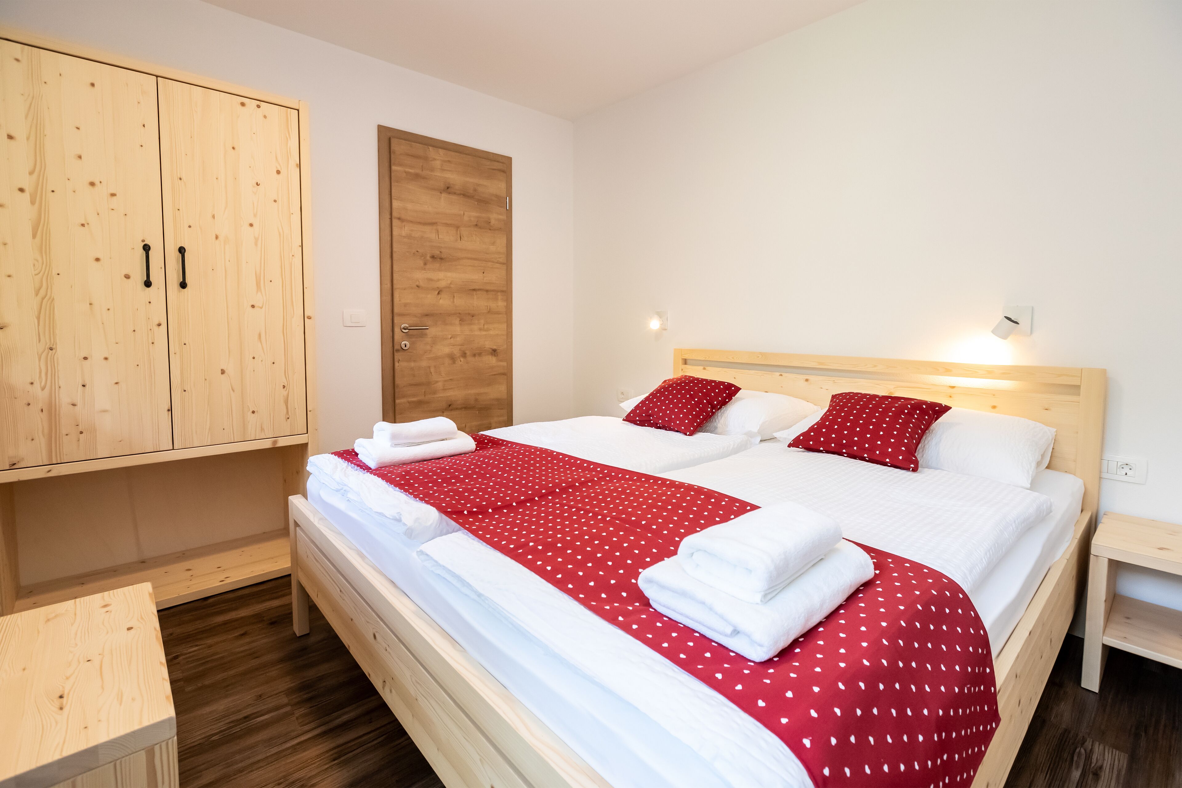 Une chambre à coucher avec un lit en bois, du linge de lit blanc et une couverture à pois rouges.