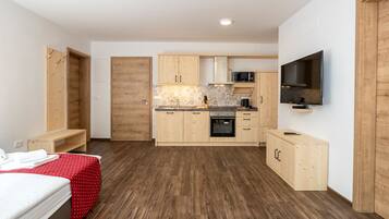 Habitación de hotel pequeña con kitchenette, una cama con colcha roja de lunares y un televisor montado en la pared.