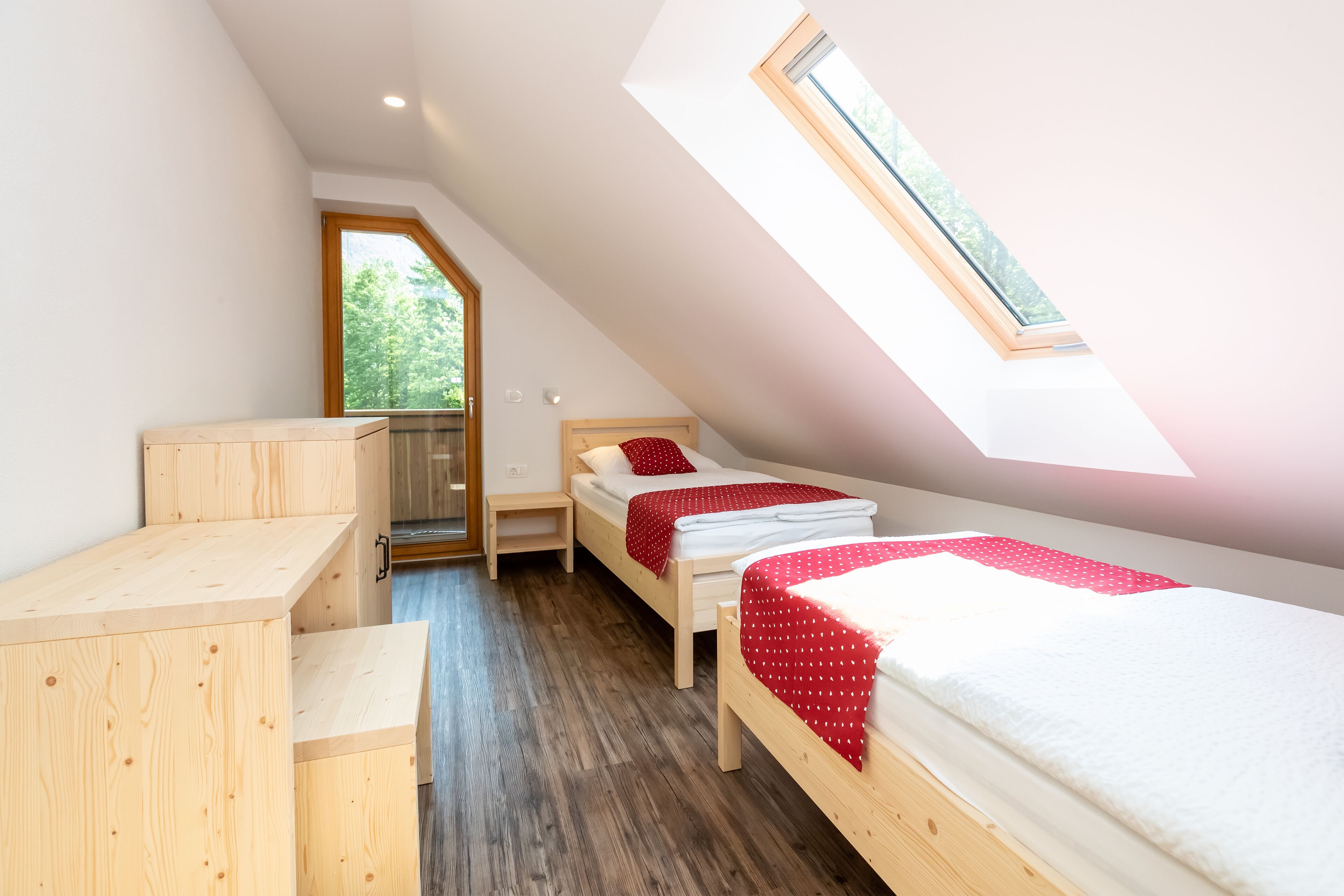 A small, well-lit room with a sloped ceiling, wooden furniture, and a window providing natural light.
