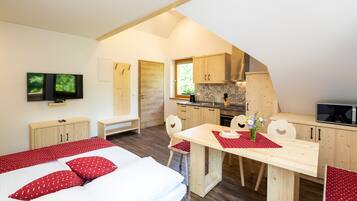 Ein Schlafzimmer mit Bett, Fernseher und einer Küchenzeile mit Holzausbau und Fenster.