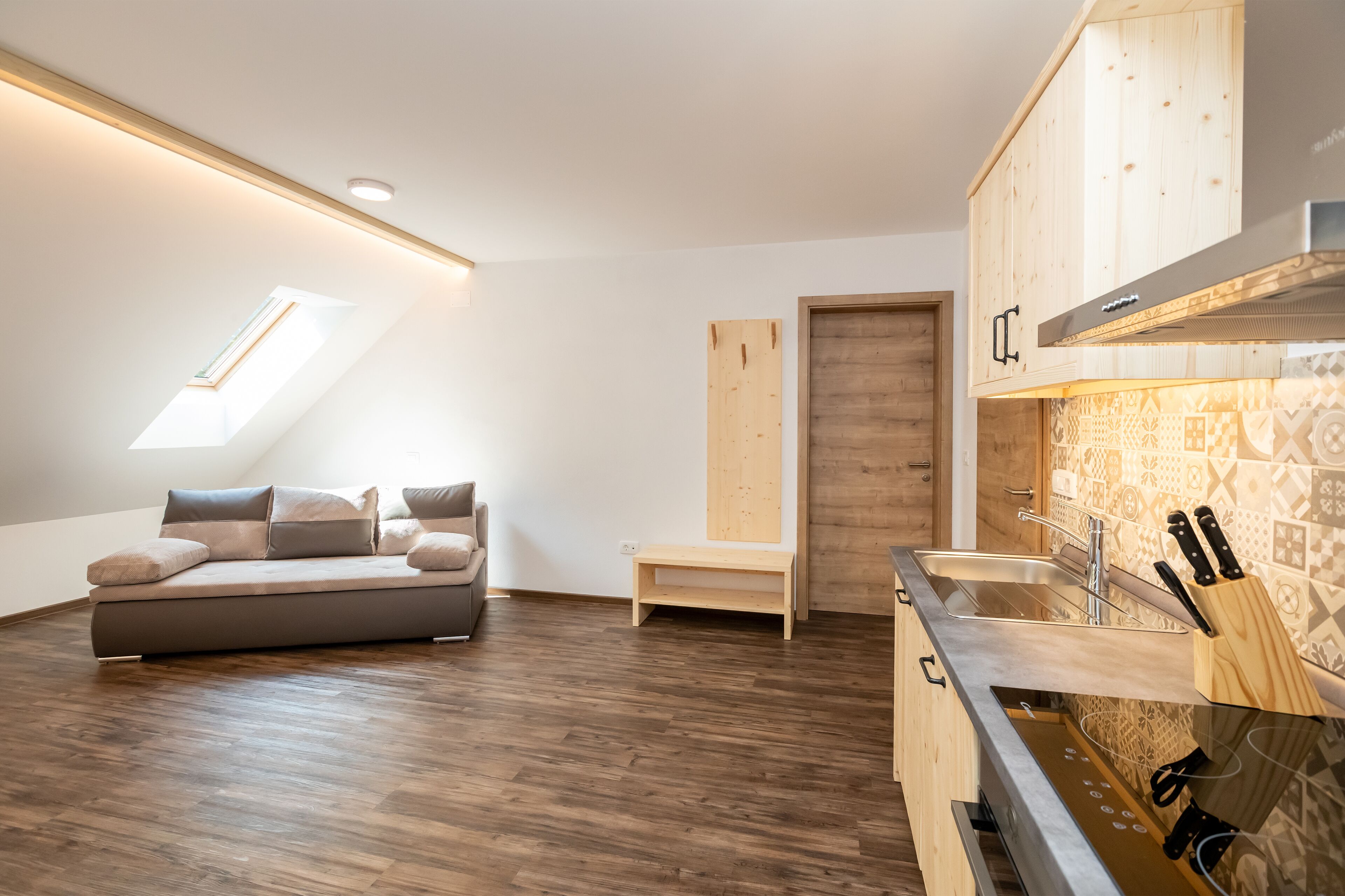 A modern loft apartment with a loft bed, a kitchen with wooden cabinets, and a skylight.