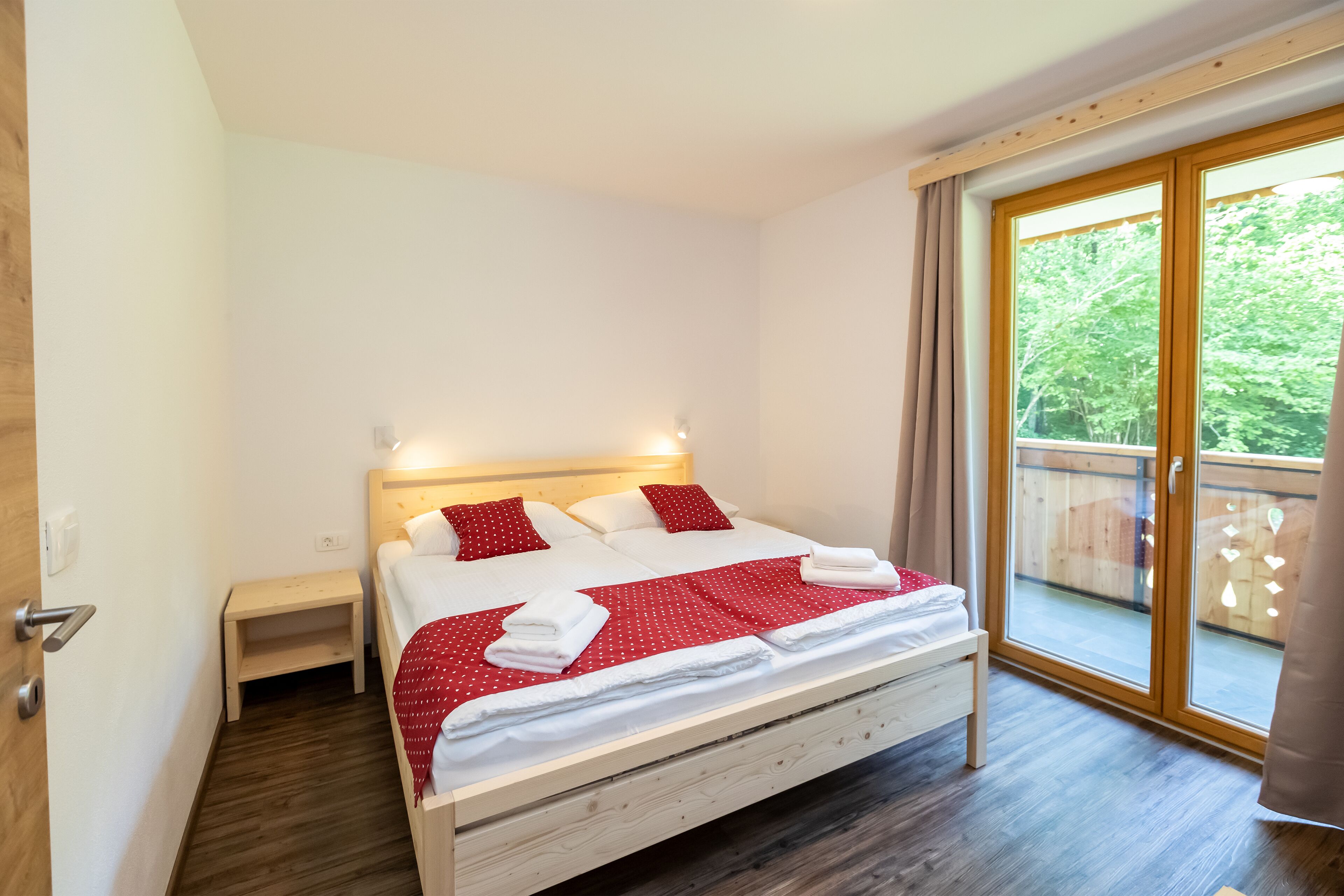 A bedroom with a wooden bed, white bedding, a nightstand, and a sliding glass door to a balcony.