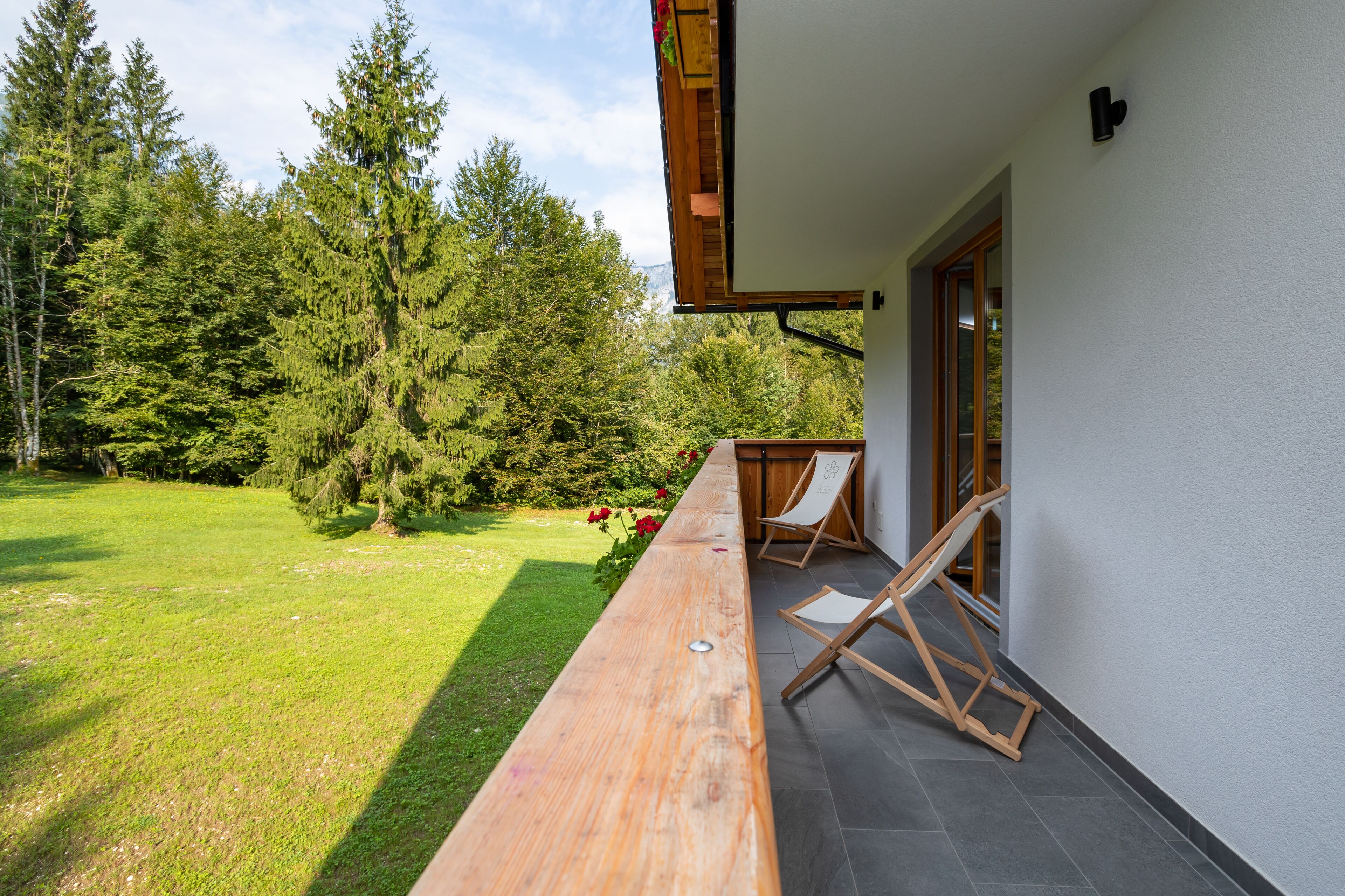 Une terrasse en bois offrant une vue sur une pelouse verdoyante et luxuriante ainsi que sur de grands arbres.