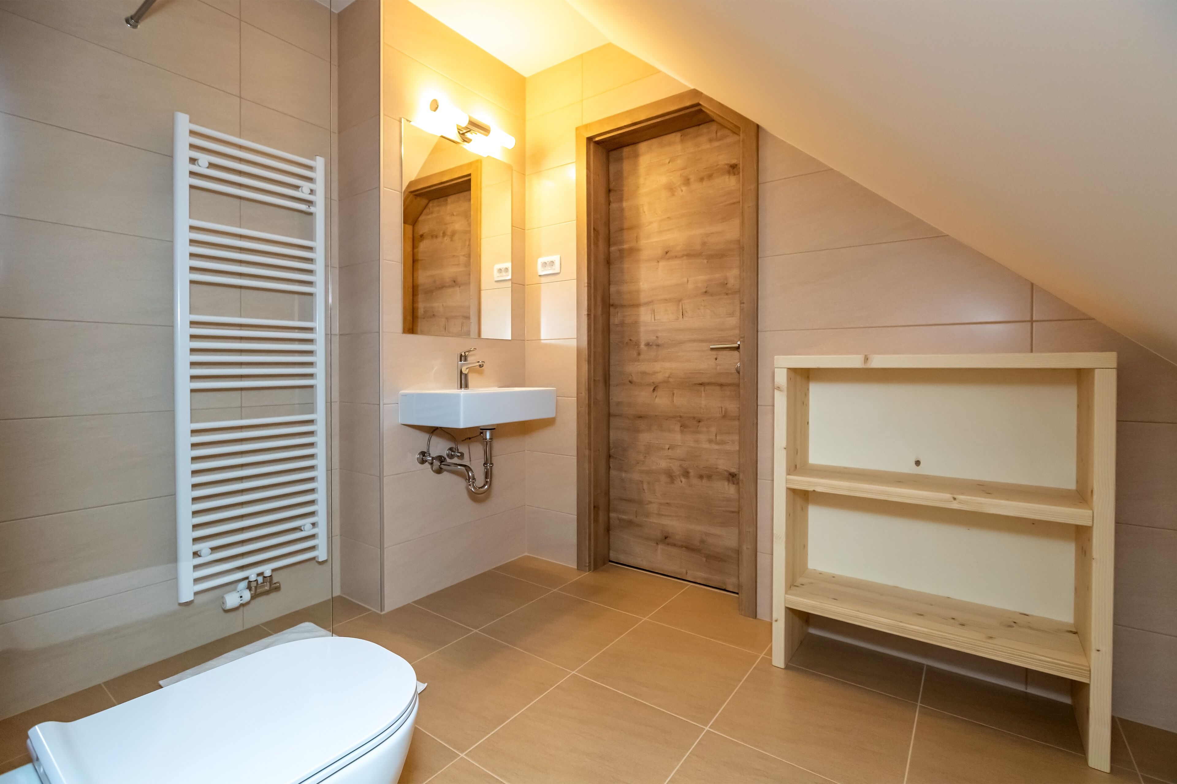 A bathroom with a white toilet, a sink with a mirror, a wooden door, and a white radiator.