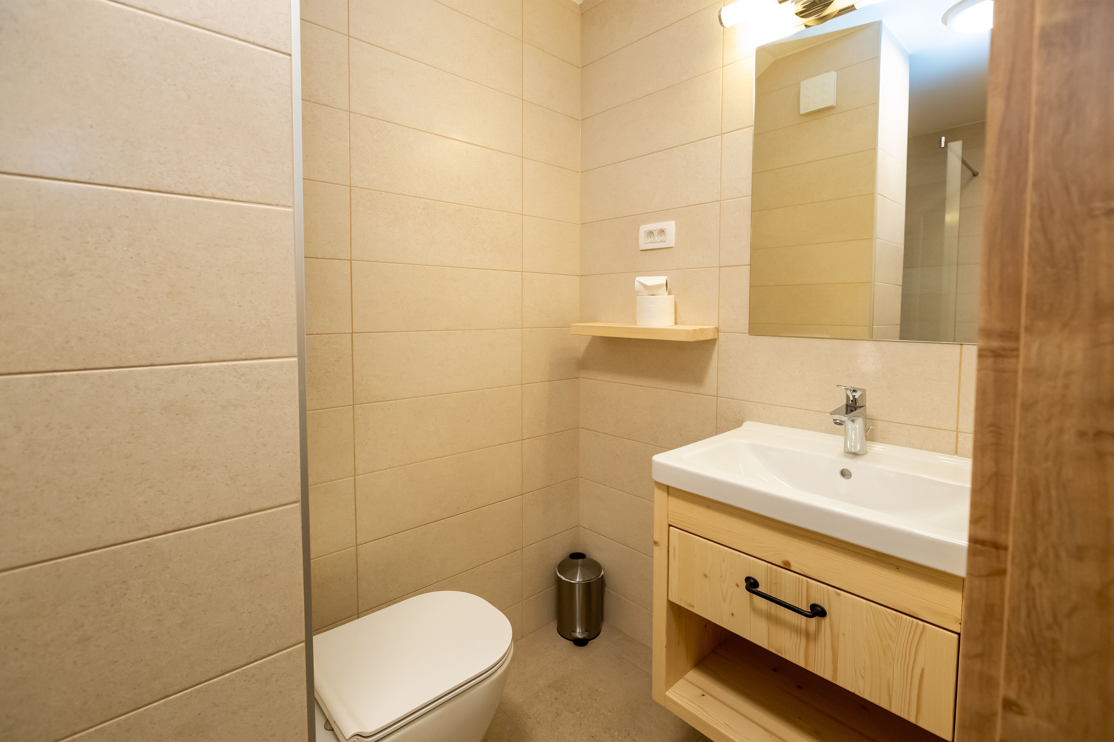 A bathroom with a toilet, sink, mirror, and a trash can.