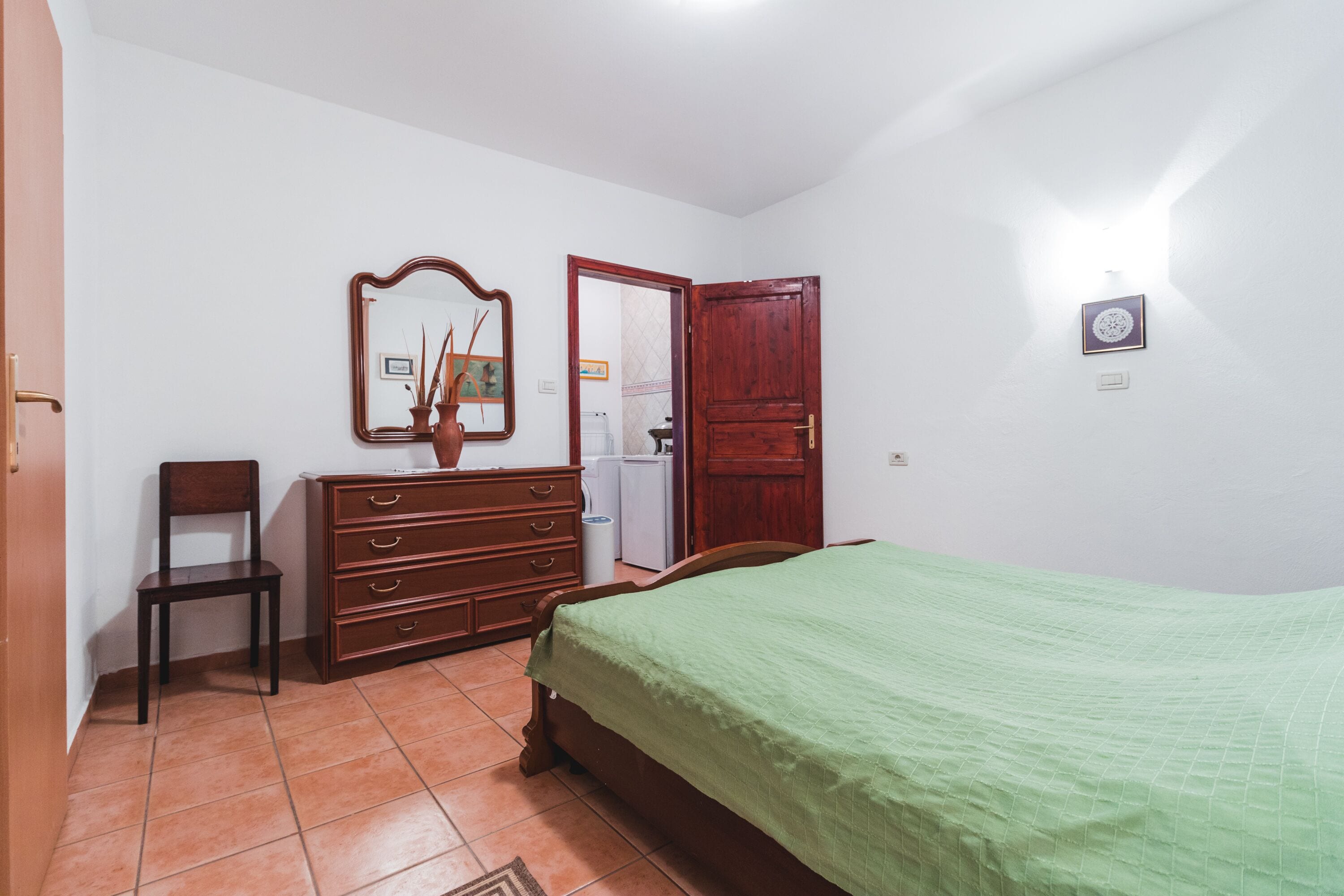 Ein Schlafzimmer mit einem Bett, einem Schminktisch, einem Sessel, einem Spiegel und einer Tür.