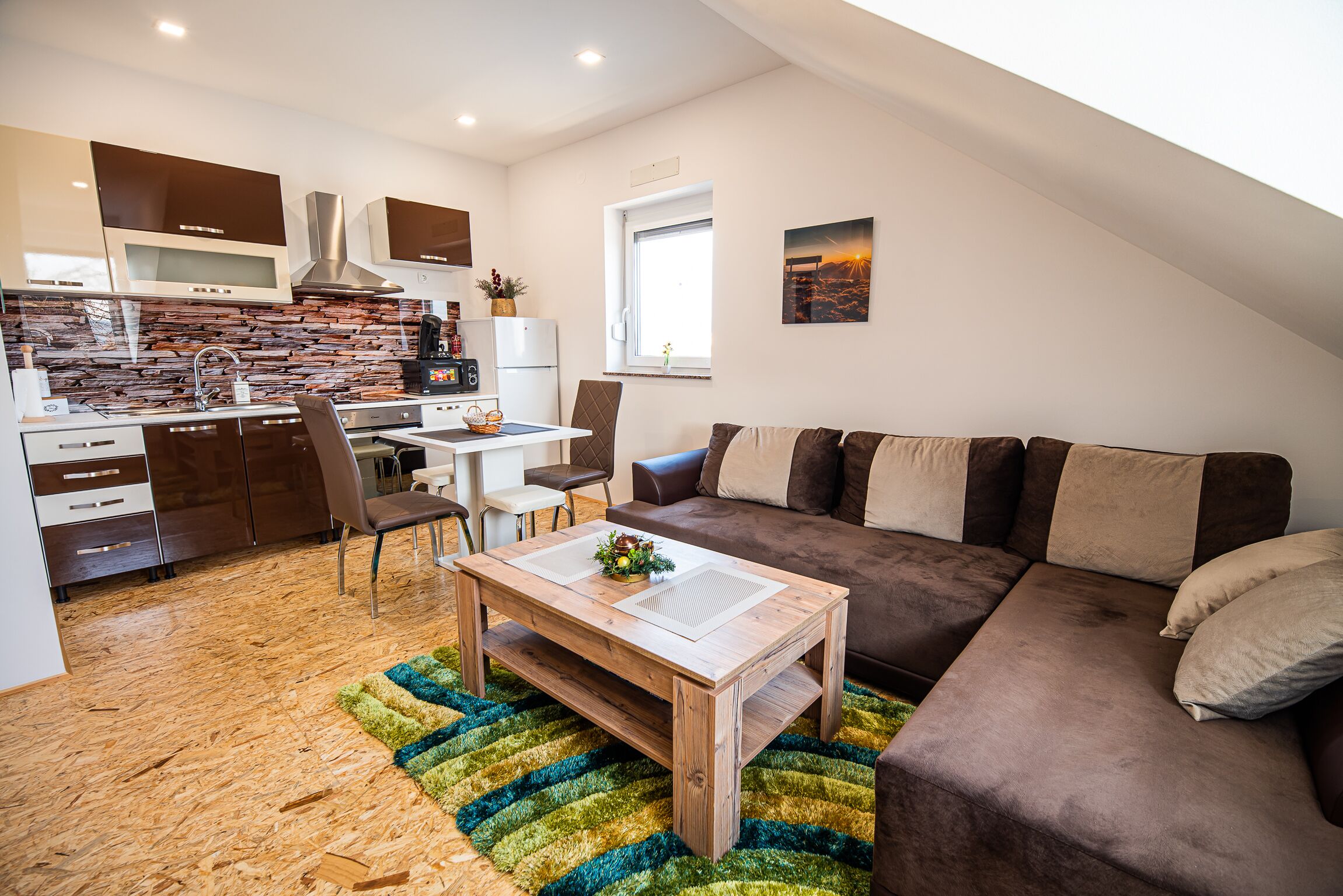 Une cuisine moderne dotée d’un four et d’un micro-ondes encastrés, un coin repas avec une table et des chaises, et un espace de vie avec un canapé et une table basse.
