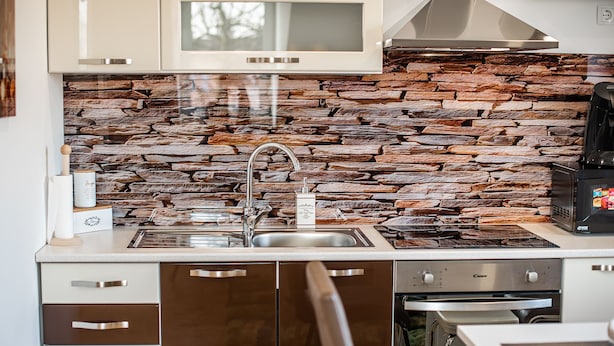 Een moderne keuken met een stenen spatwand, roestvrijstalen apparatuur en een inbouwoven.