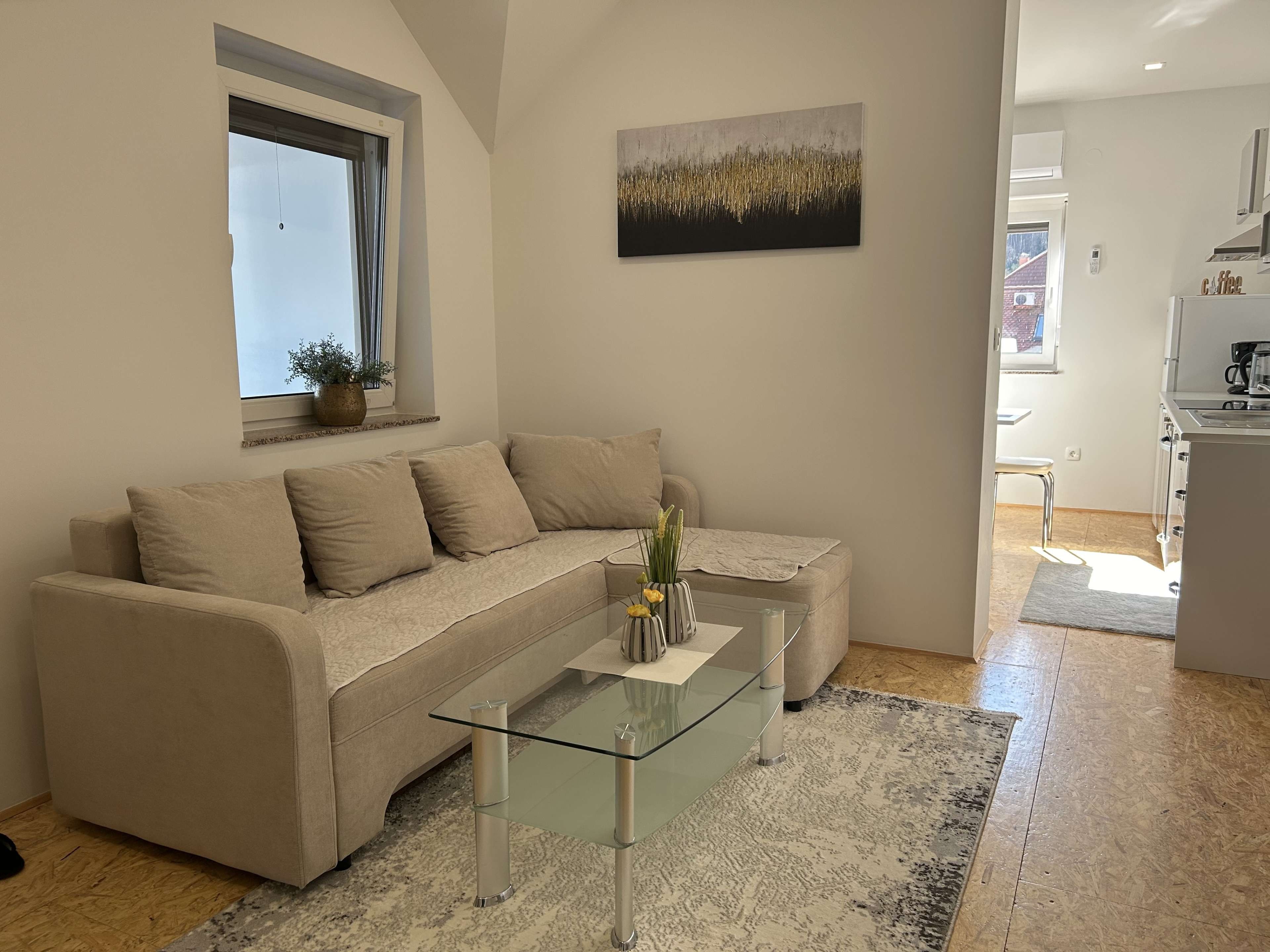 Een moderne woonkamer met een beige bank, een glazen salontafel en een schilderij aan de muur.