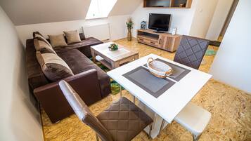 A modern living room with a brown sofa, a white coffee table, and a dining area with a white table and brown chairs.
