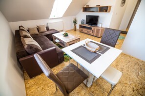 Una sala moderna con un sofá marrón, una mesa de centro blanca y un comedor con una mesa blanca y sillas marrones.