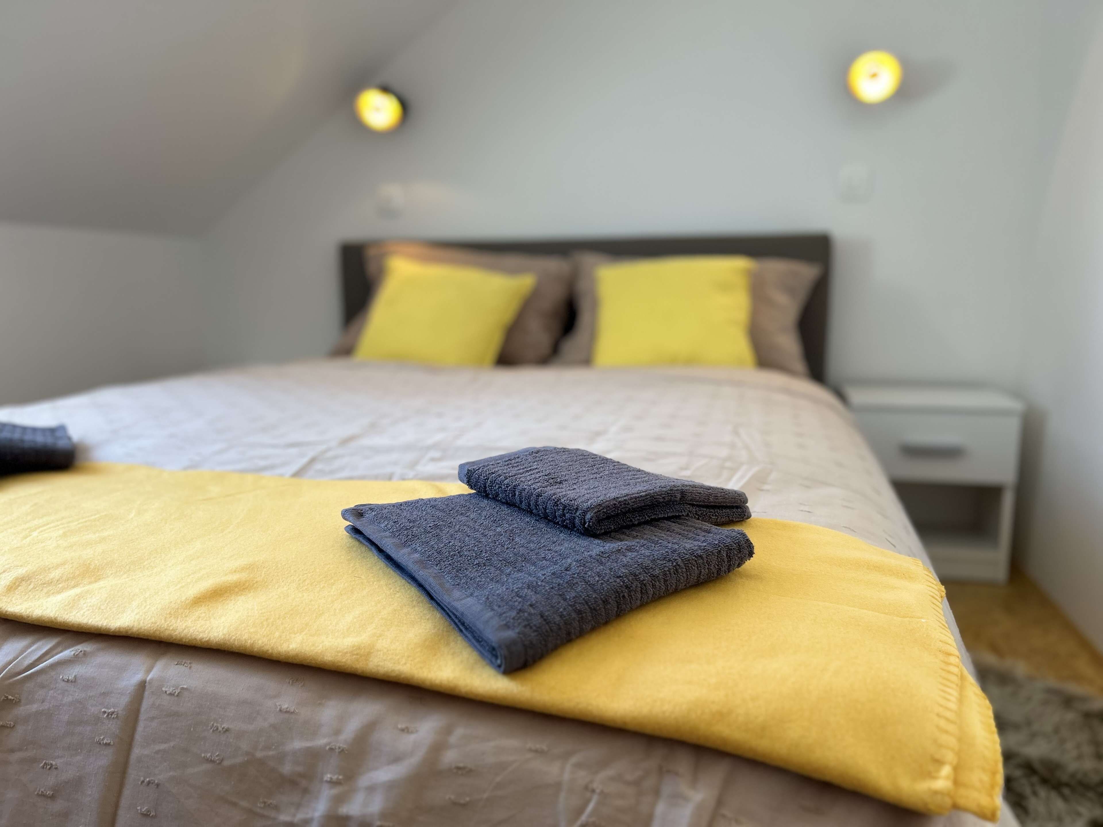 A neatly made bed with a yellow and gray blanket, two pillows, and folded towels.
