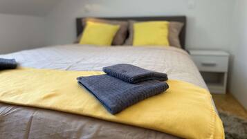 A neatly made bed with a yellow and gray blanket, two pillows, and folded towels.