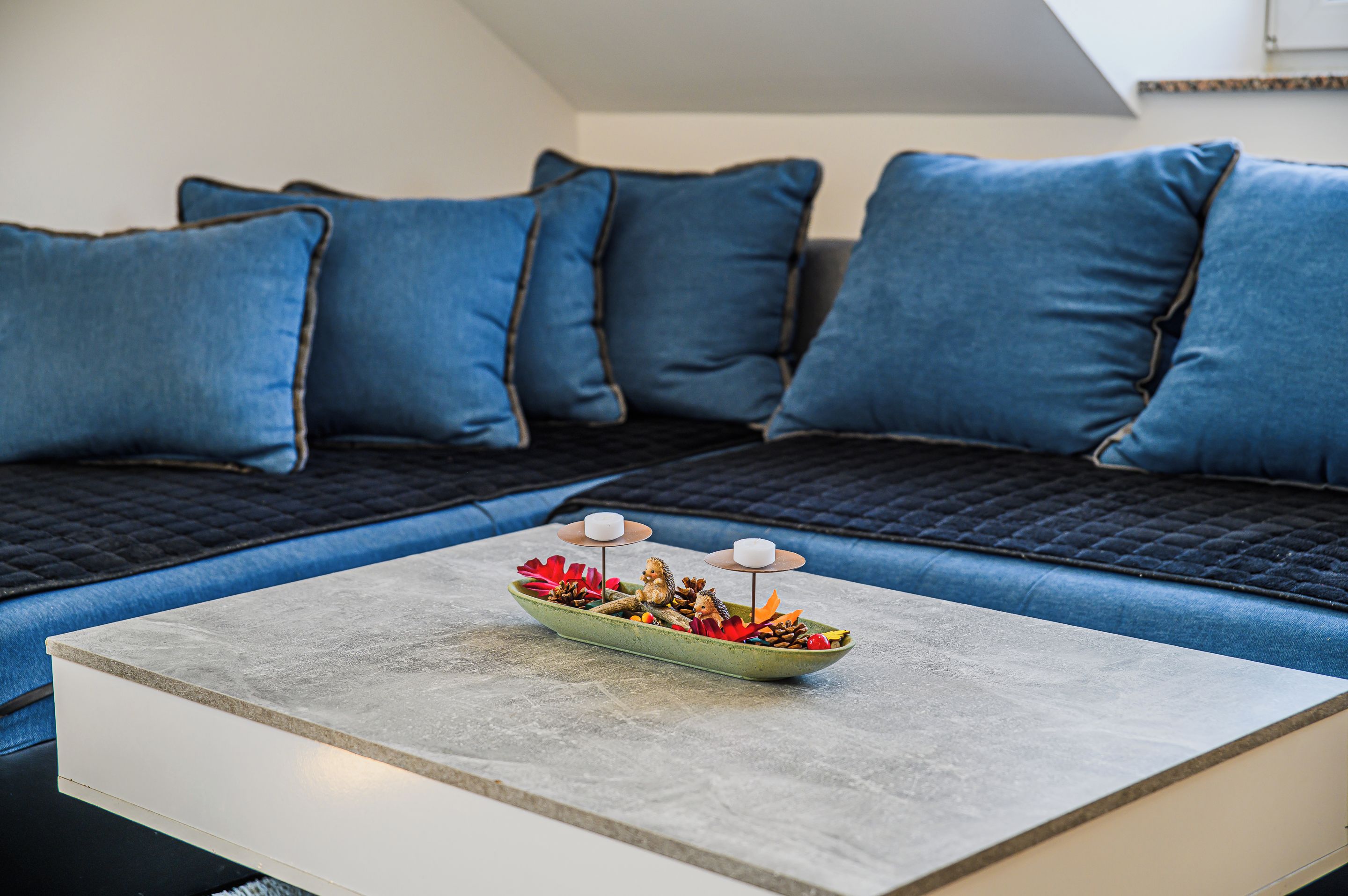 Un salon moderne avec un canapé d’angle, une petite table agrémentée d’un élément décoratif central et une vue sur l’extérieur.