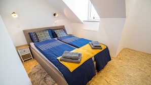 Een slaapkamer met een hoogslaper, een klein nachtkastje, een vloerkleed en een raam met uitzicht.
