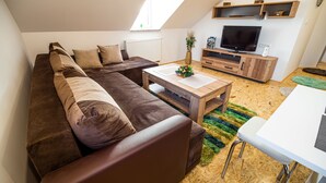 Een moderne woonkamer met een hoekbank, een houten salontafel, een televisie en een kleine eethoek.