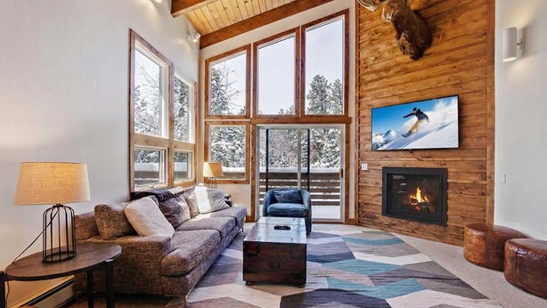 A cozy living room with a large window, a fireplace, and a mounted television. - Mountain Chalet Just Blocks from Gondola & Main St (Breckenridge)