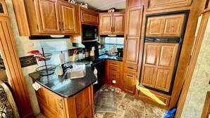 A compact kitchen with wooden cabinets, a black countertop, and a stainless steel sink.