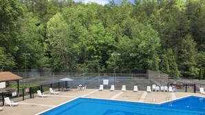 A swimming pool with a fence, lounge chairs, and a tennis court in the background.