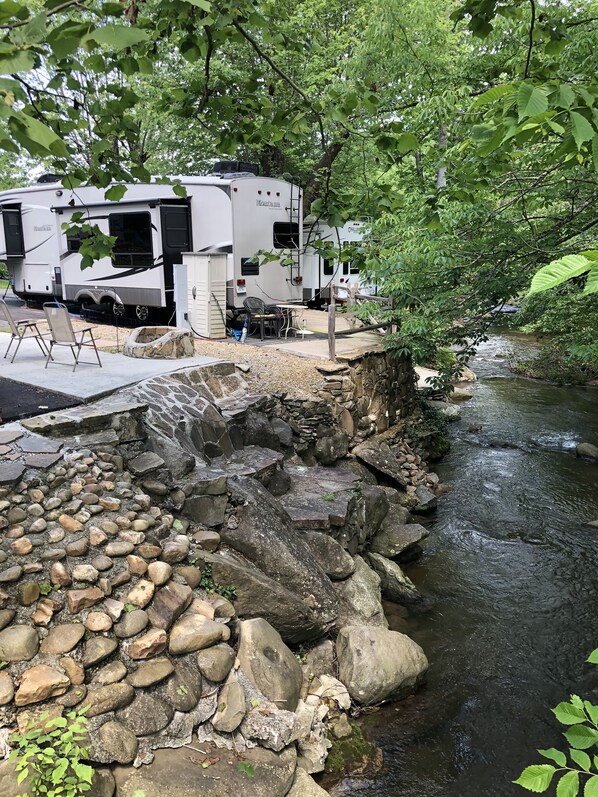 A campsite with RVs, a stone retaining wall, and a stream.