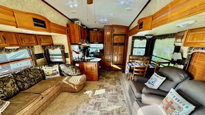 A spacious RV interior with a kitchen area, a seating area with a sofa and chairs, and a dining table.
