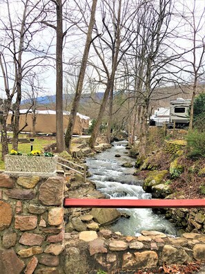 A stone bridge over a flowing stream, surrounded by trees and a distant RV campsite. -  Brand New List!! Beautiful RV on Creekfront lot. Amenities galore. Lot 311 (Gatlinburg)