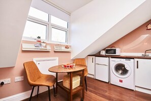 A compact kitchen with a washing machine, a microwave, and a small dining table with chairs.