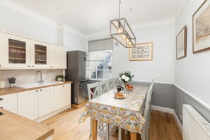 Une cuisine moderne avec des meubles blancs, un réfrigérateur en acier inoxydable et une table à manger recouverte d’une nappe à motifs floraux.