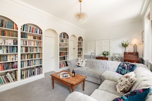 Un salon spacieux avec un grand canapé d’angle, une table basse en bois et de nombreuses étagères remplies de livres.