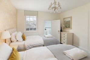 Une chambre avec deux lits, une commode, un miroir et une fenêtre donnant sur des immeubles.