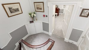 Un escalier avec une rampe en bois, des murs blancs et des tableaux encadrés.
