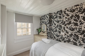 Een slaapkamer met een bed, een dressoir, een raam met zonwering en een bloemenbehang.
