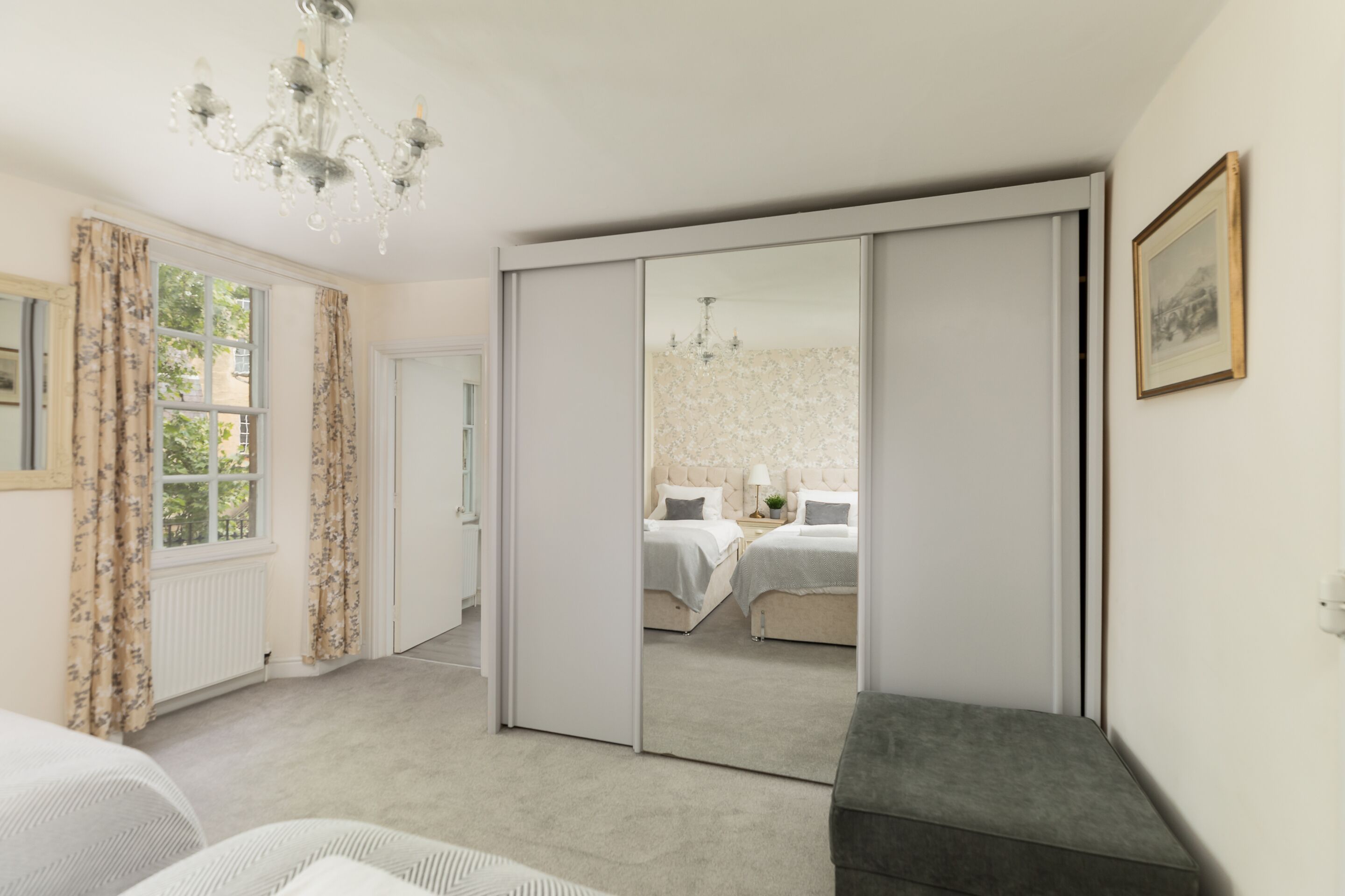 A bedroom with a large mirror, a bed, a bench, and a chandelier.